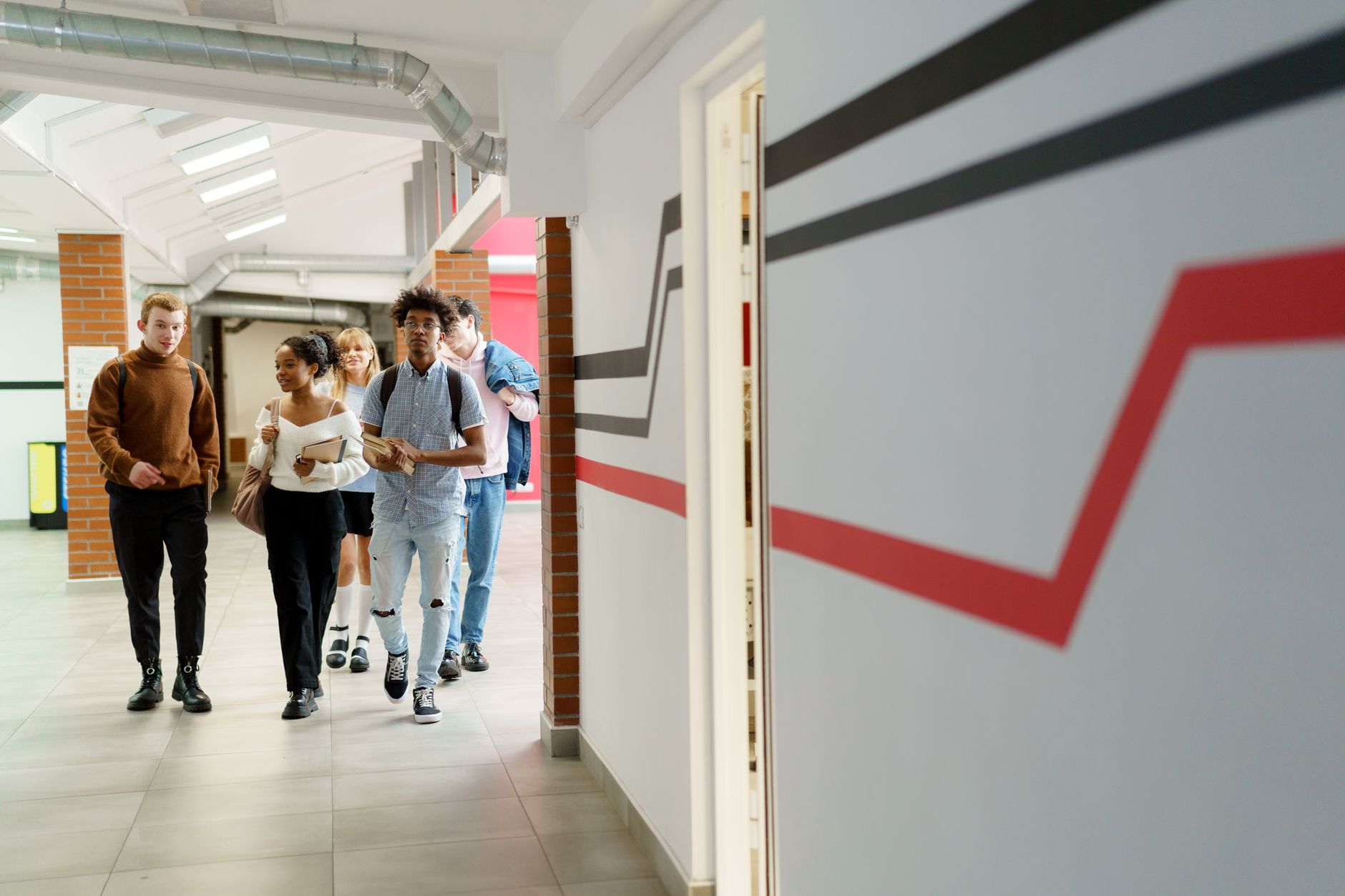 Plusieurs jeunes élèves marchant dans un couloir d’école avec des sacs et des livres.