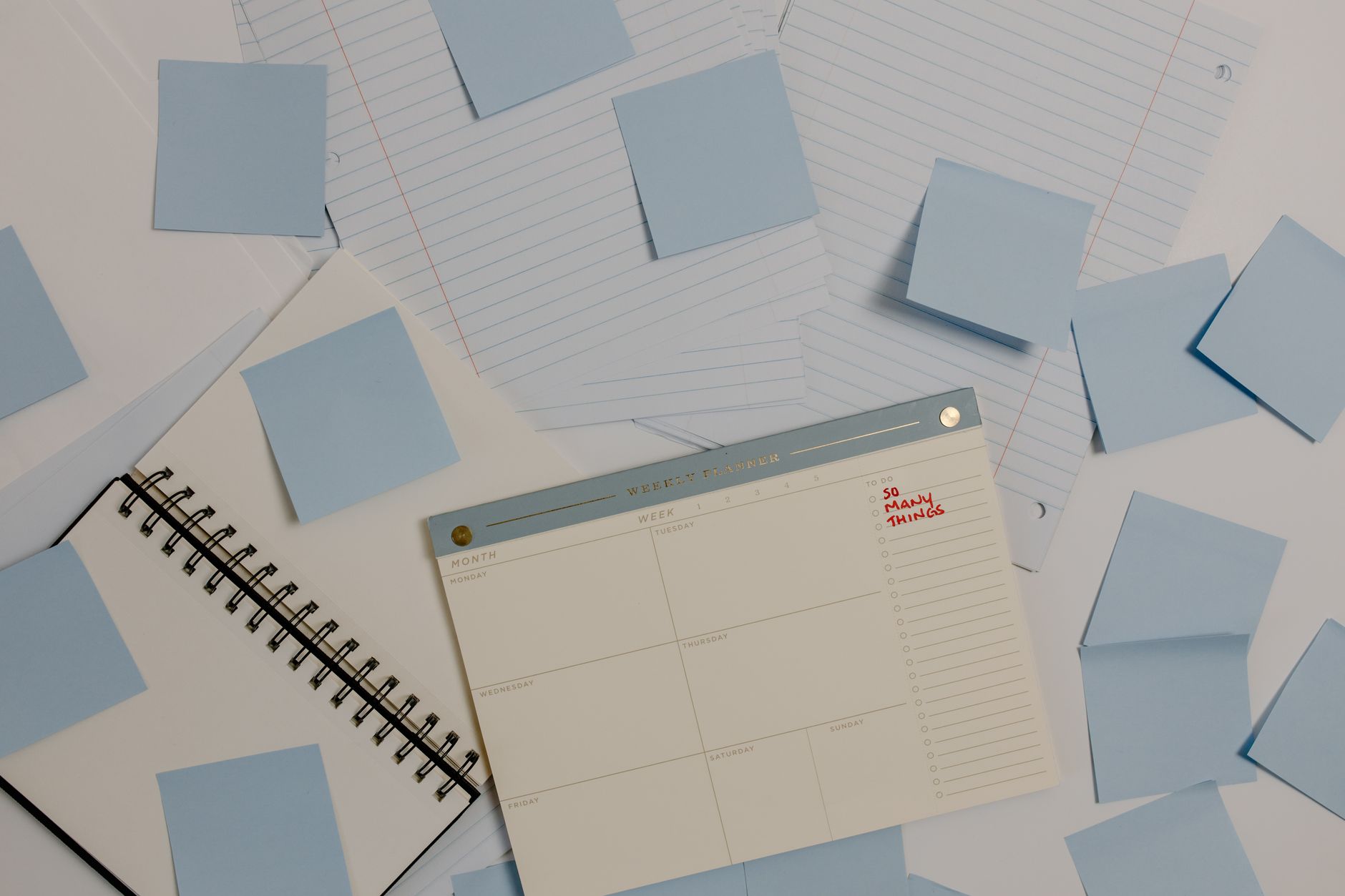 Vue de dessus de feuilles lignées, de notes adhésives bleues, d’un carnet à spirale et d’un planificateur hebdomadaire annoté.